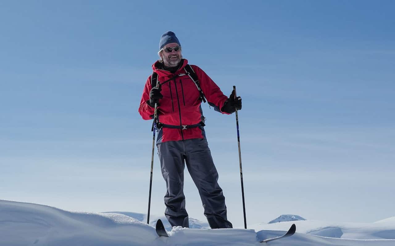 Person på ski i snødekte fjell med klar blå himmel i bakgrunnen.